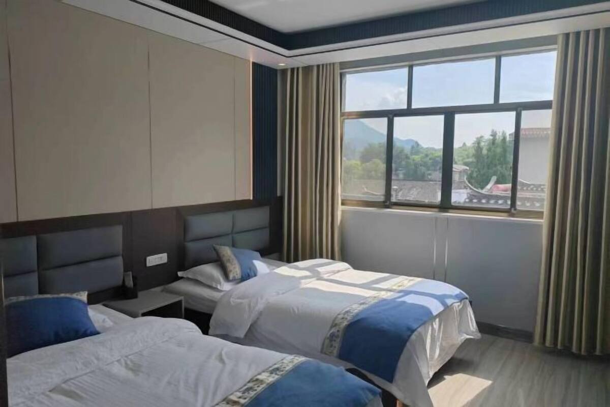 A hotel room with two beds, a large window with curtains, and a view of a traditional building outside.