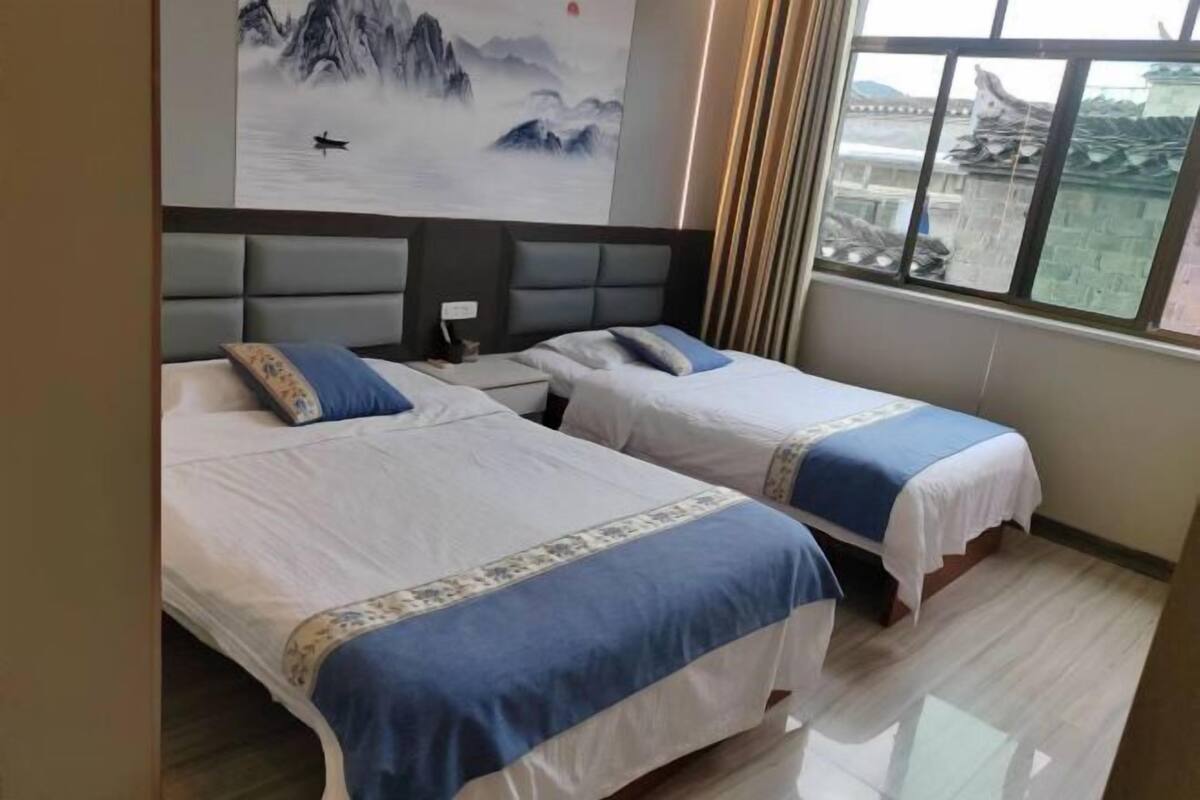 A hotel room with two beds, a large window with a view of traditional architecture, and a painting on the wall.