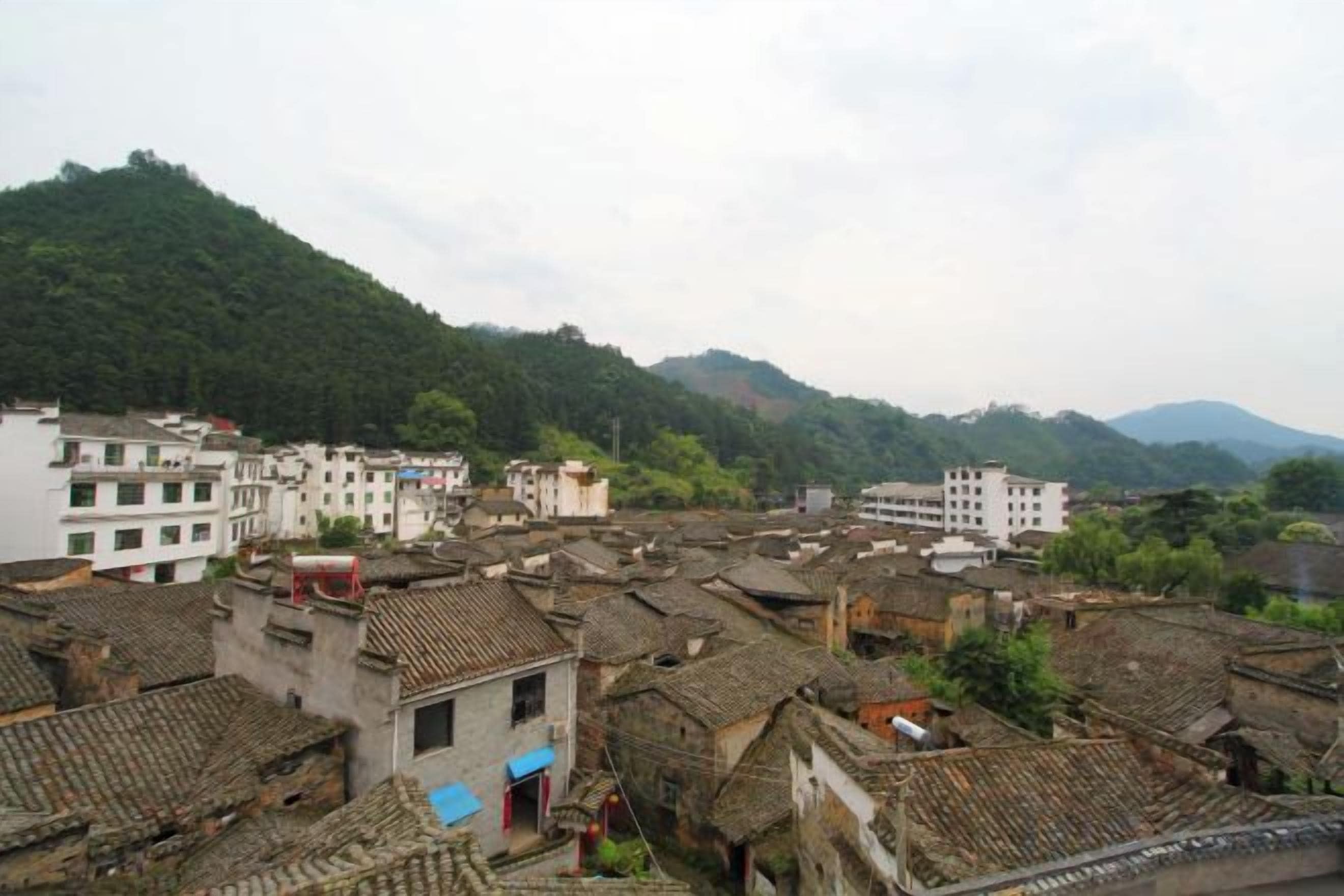 Un pueblo tradicional con edificios de tejados de teja y una colina al fondo, con una mezcla de construcciones residenciales y comerciales.