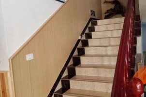 Una escalera con barandilla de madera y peldaños alfombrados en color beige.