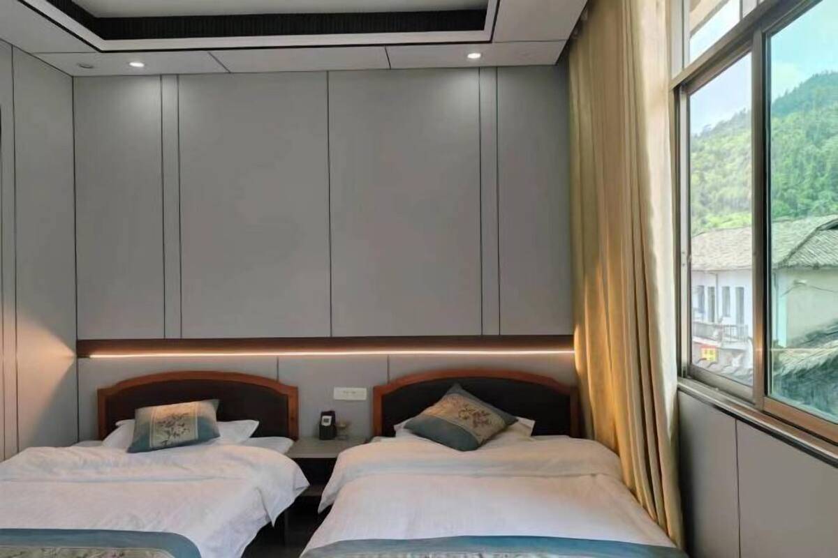 A hotel room with two beds, a wooden headboard, a nightstand, and a window with curtains.