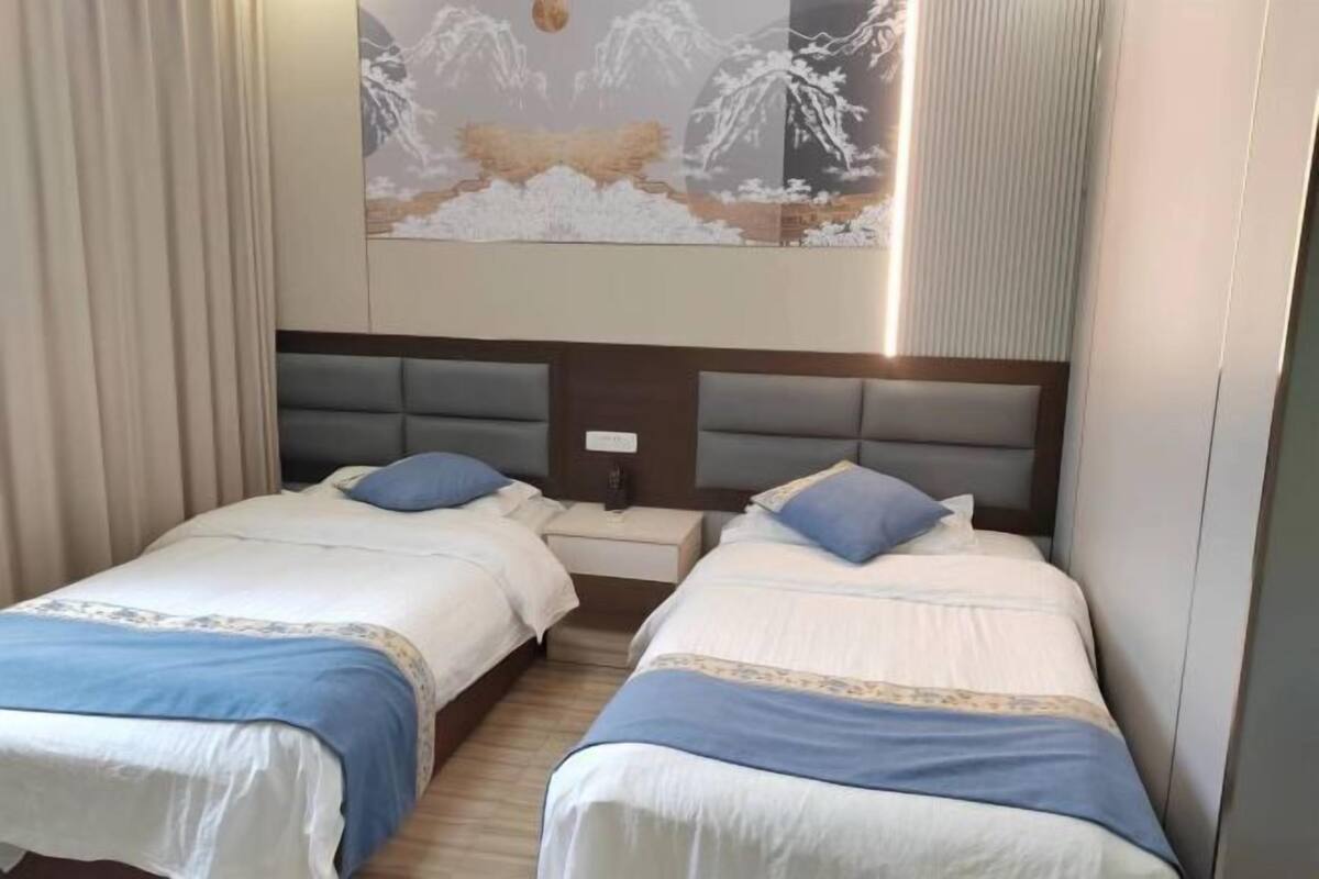 A hotel room with two beds, a nightstand, and a painting of a snowy mountain scene.