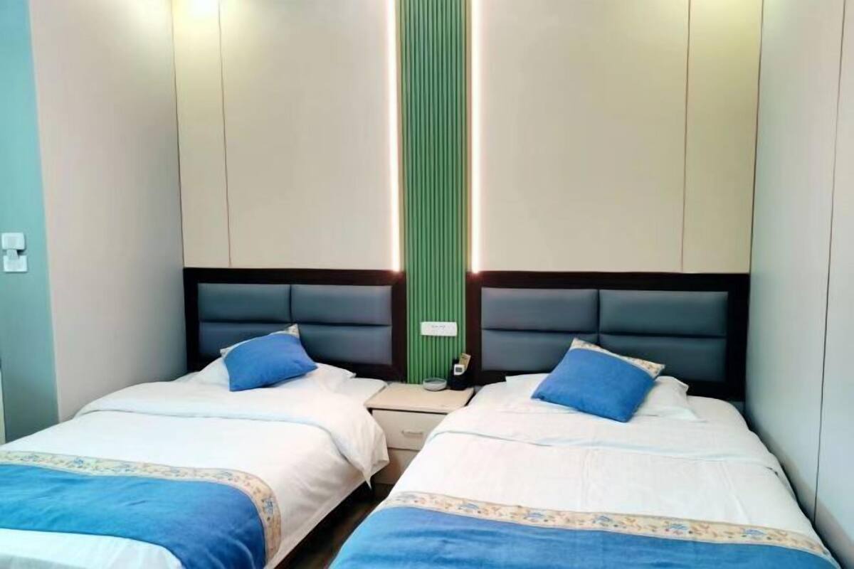 A hotel room with two beds, each with a blue pillow and a white bedspread.