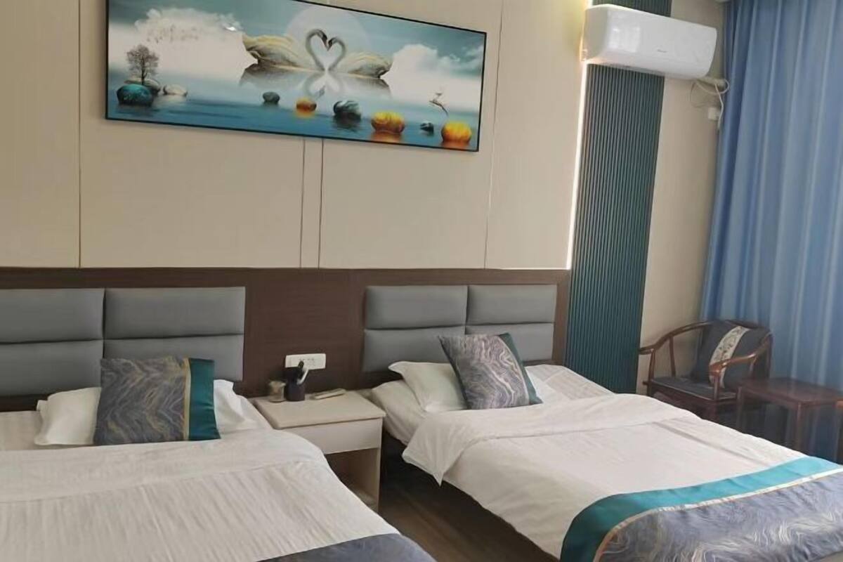 A hotel room with two beds, a painting of a swan on the wall, and an air conditioning unit.