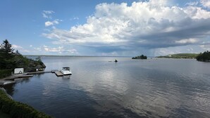 A calm lake with boats docked at a pier, surrounded by greenery and distant islands.