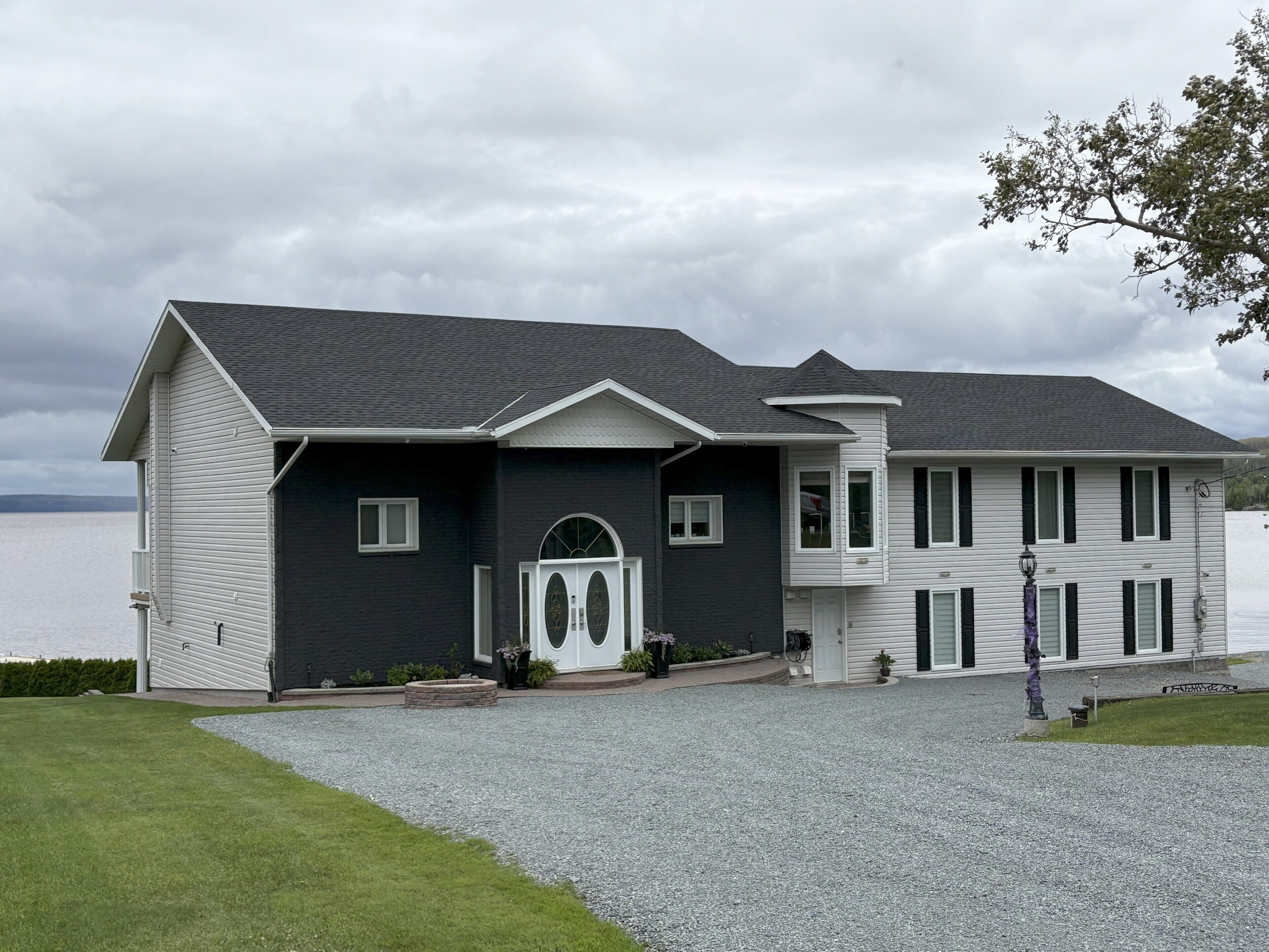A two-story house with a dark exterior, a white front door, and a gravel driveway.