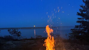 A campfire at dusk with a lake and trees in the background.