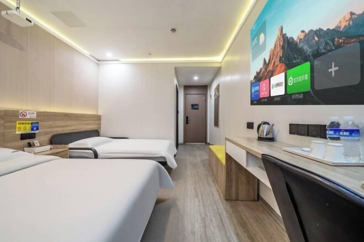A hotel room with two beds, a desk, a chair, a TV, and a bathroom door.