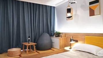 Quarto de hotel moderno com cama, mesa de cabeceira, abajur e um grande puff.