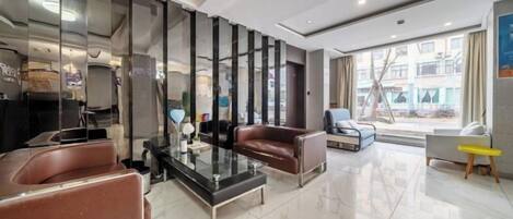 A modern hotel lobby with a reception desk, seating area, and large windows.