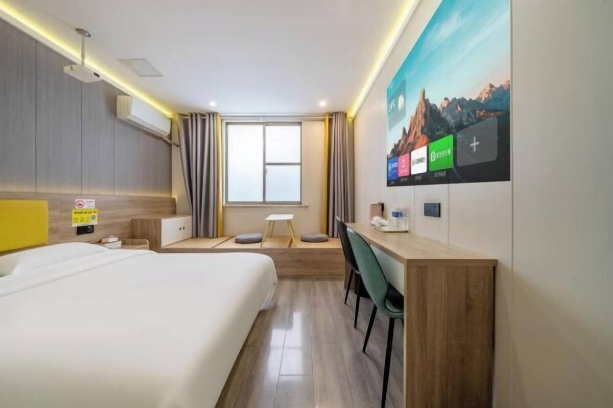 A hotel room with a bed, desk, chair, and a large window.