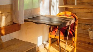 A wooden interior with a sloped ceiling, a window with curtains, a chair, and a table.