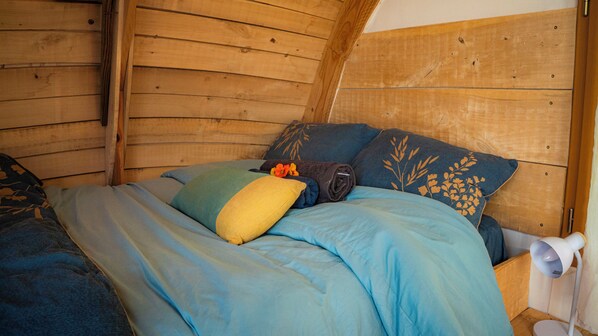 A wooden cabin-style room with a bed, pillows, and a nightstand.