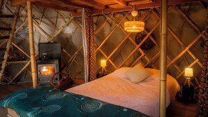 A cozy room with a bed, a small wooden stove, and a hanging light fixture.