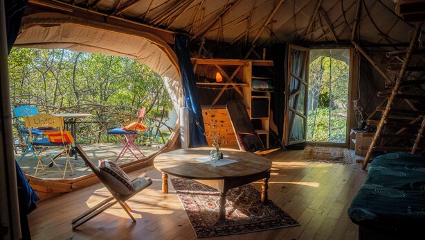 A tent with a wooden table, chairs, and a view of trees.