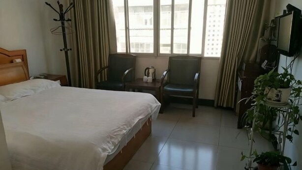 Une chambre d’hôtel avec un lit, deux chaises, une petite table et une plante en pot.