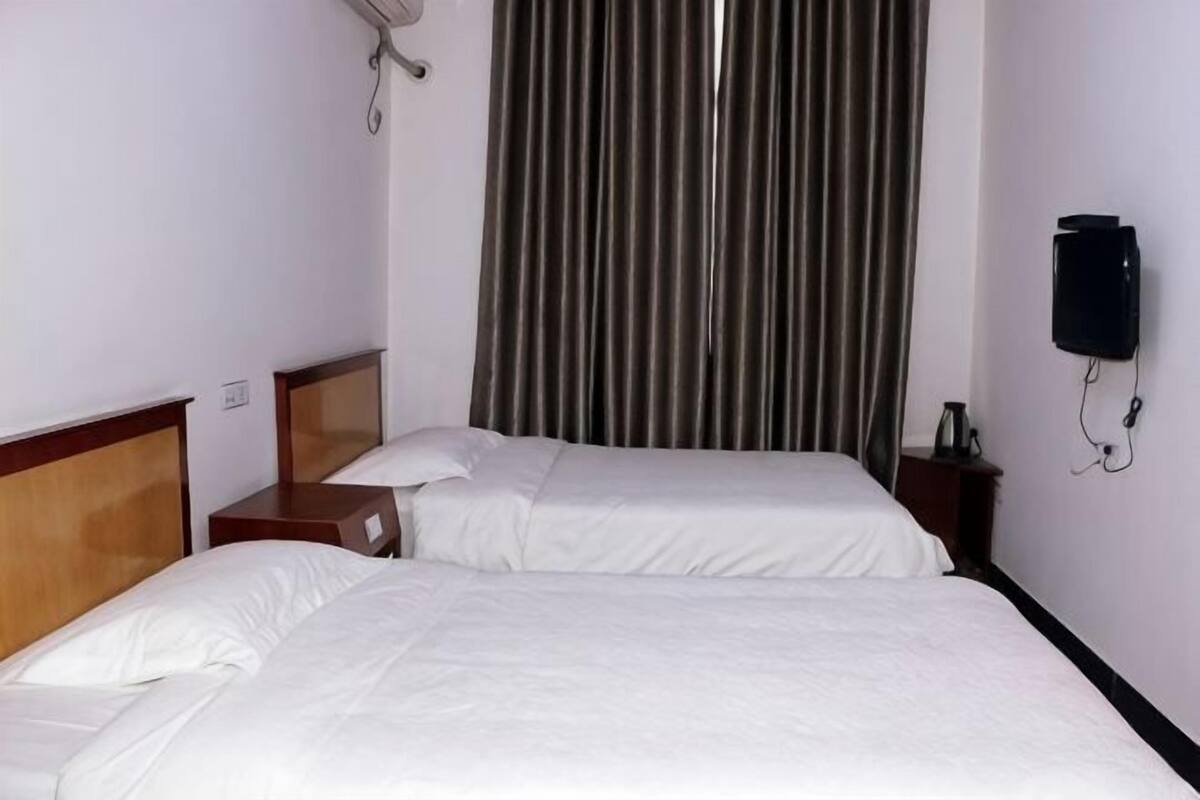 Una habitación de hotel con dos camas, una cortina, un teléfono montado en la pared y una mesita de noche.