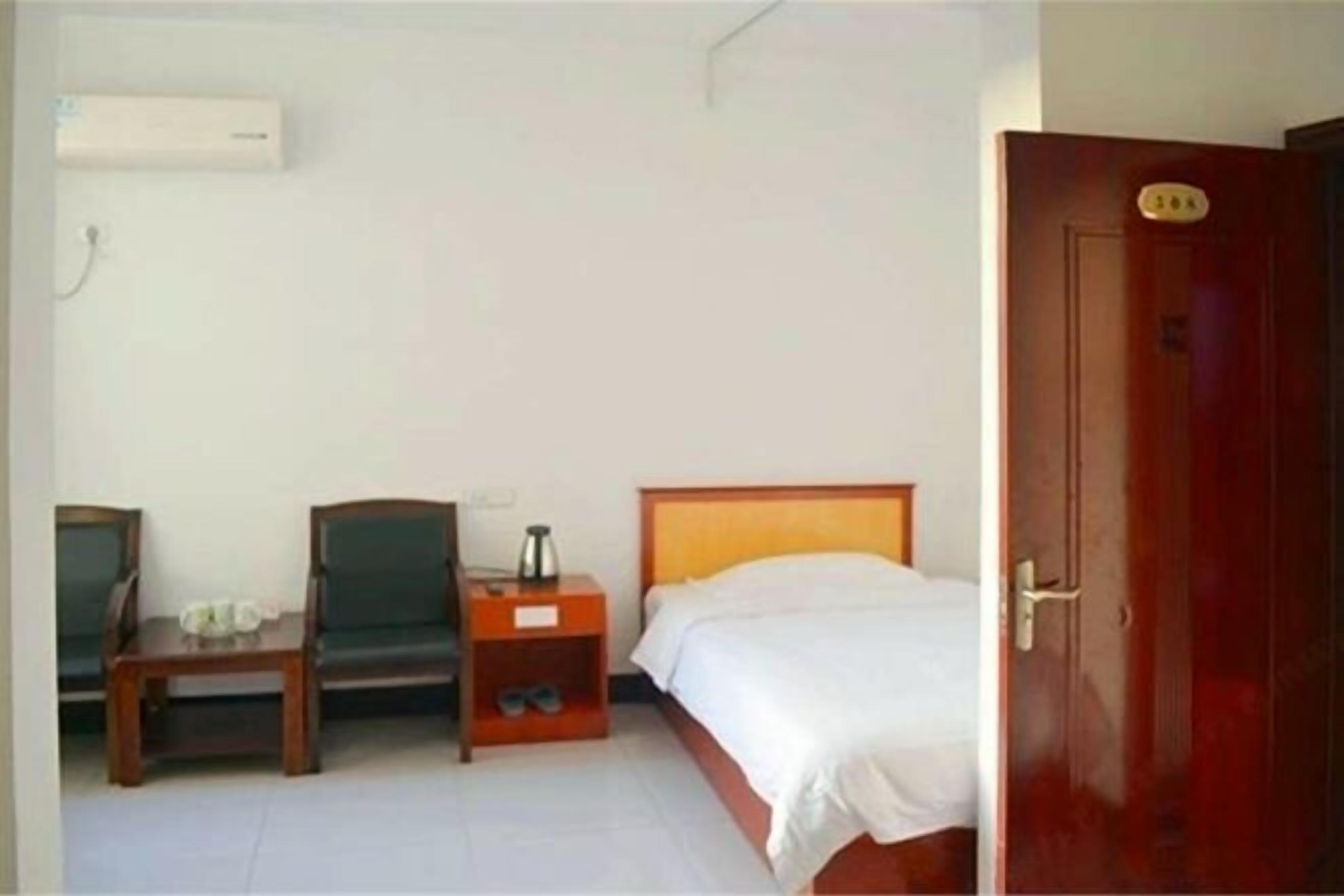 Un letto singolo con testiera in legno, un comodino con una lampada, una sedia e una piccola mensola con un paio di scarpe.