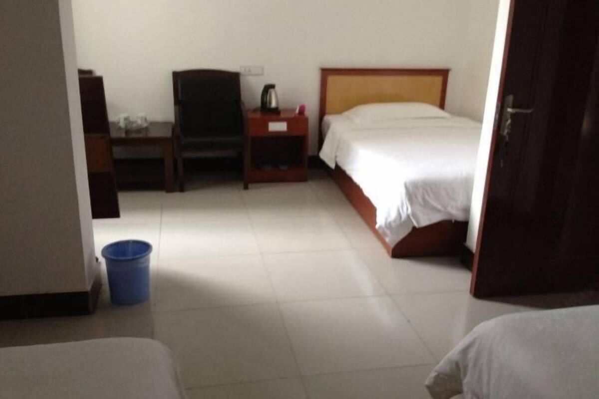 Una habitación de hotel con una cama, una silla, una mesita de noche y un cubo azul en el suelo.