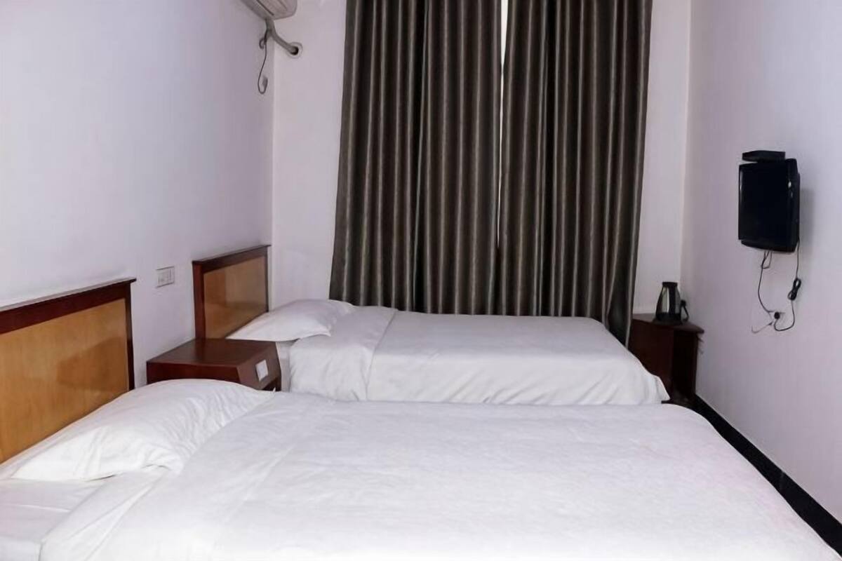 Una habitación de hotel con dos camas individuales, una mesita de noche con lámpara, un televisor en la pared y una cortina.