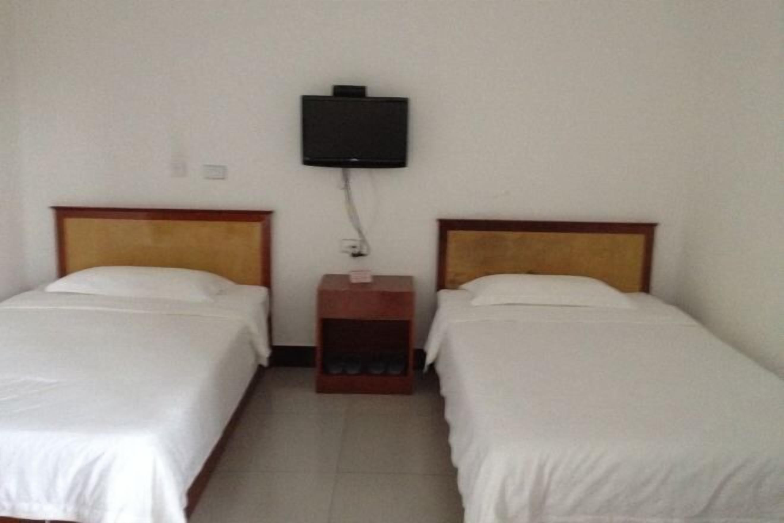 A room with two single beds, a small wooden nightstand, and a mounted television.