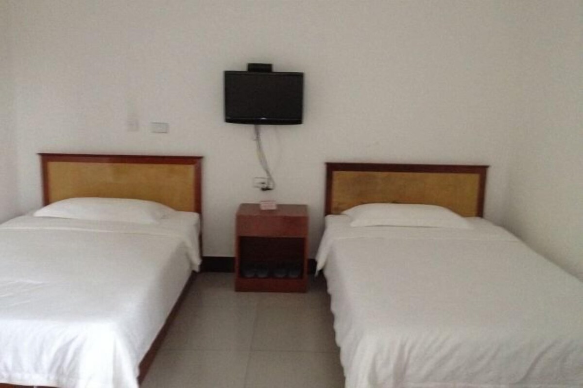 A room with two single beds, a small wooden nightstand, and a mounted television.