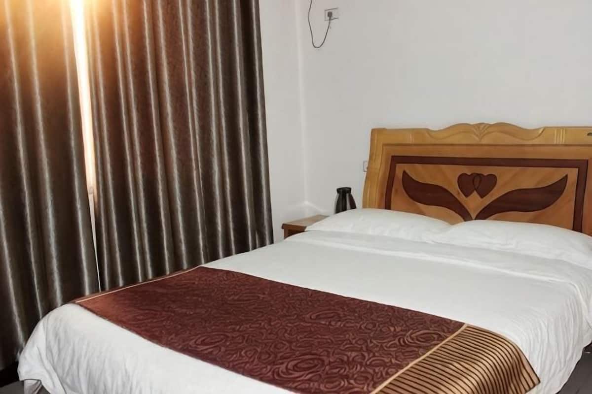 Habitación de hotel con cama, cortinas, cabecero de madera y un enchufe en la pared.