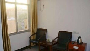Une pièce avec deux chaises, une petite table, un appareil de climatisation et une fenêtre avec des rideaux.