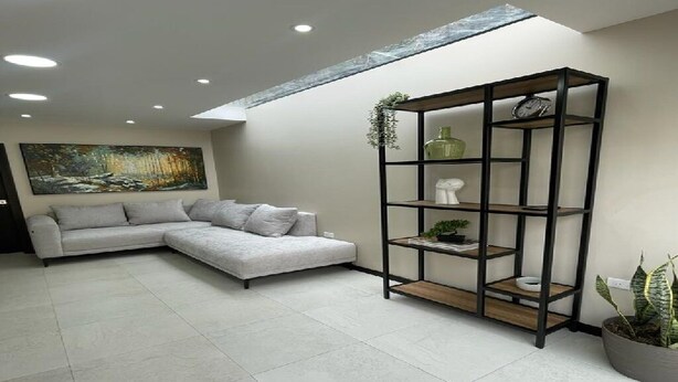 A modern living room with a sectional sofa, a tall black shelving unit with plants, and a large painting on the wall. - 2BR duplex with city views.  "Casa Colibrí" (Cuenca)