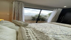 A bedroom with a large bed, a balcony with potted plants, and a view of the city. - 2BR duplex with city views.  "Casa Colibrí" (Cuenca)