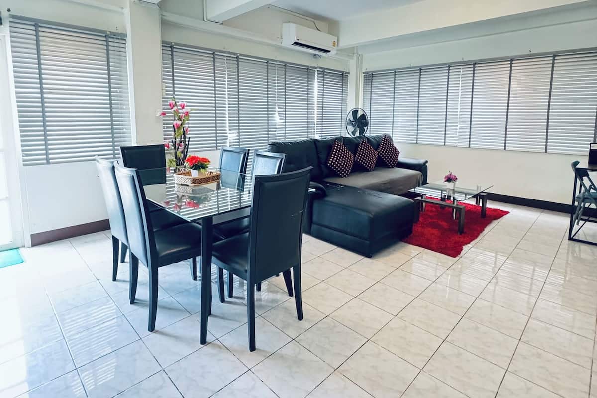 Uma sala de estar ampla com uma mesa de jantar e cadeiras, um sofá preto e um tapete vermelho.