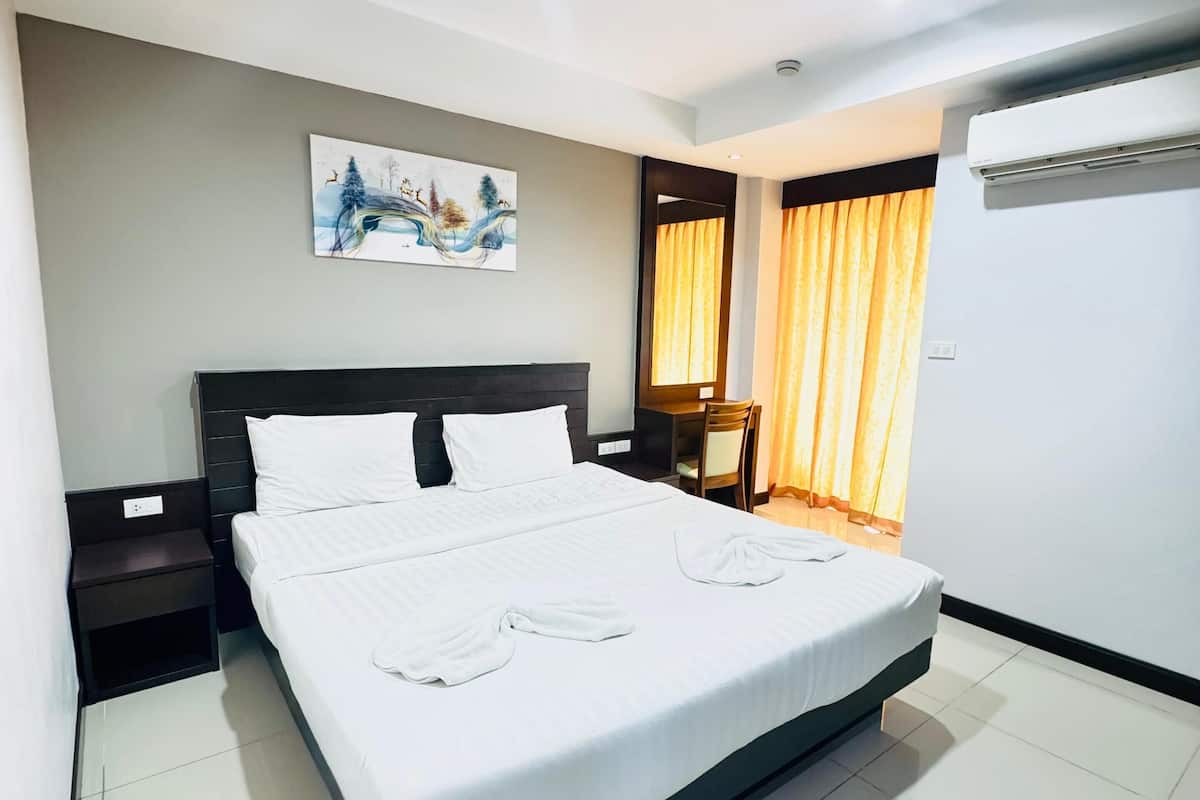 Quarto de hotel com uma cama grande, uma mesa de cabeceira, uma cadeira, um quadro na parede e um aparelho de ar condicionado.