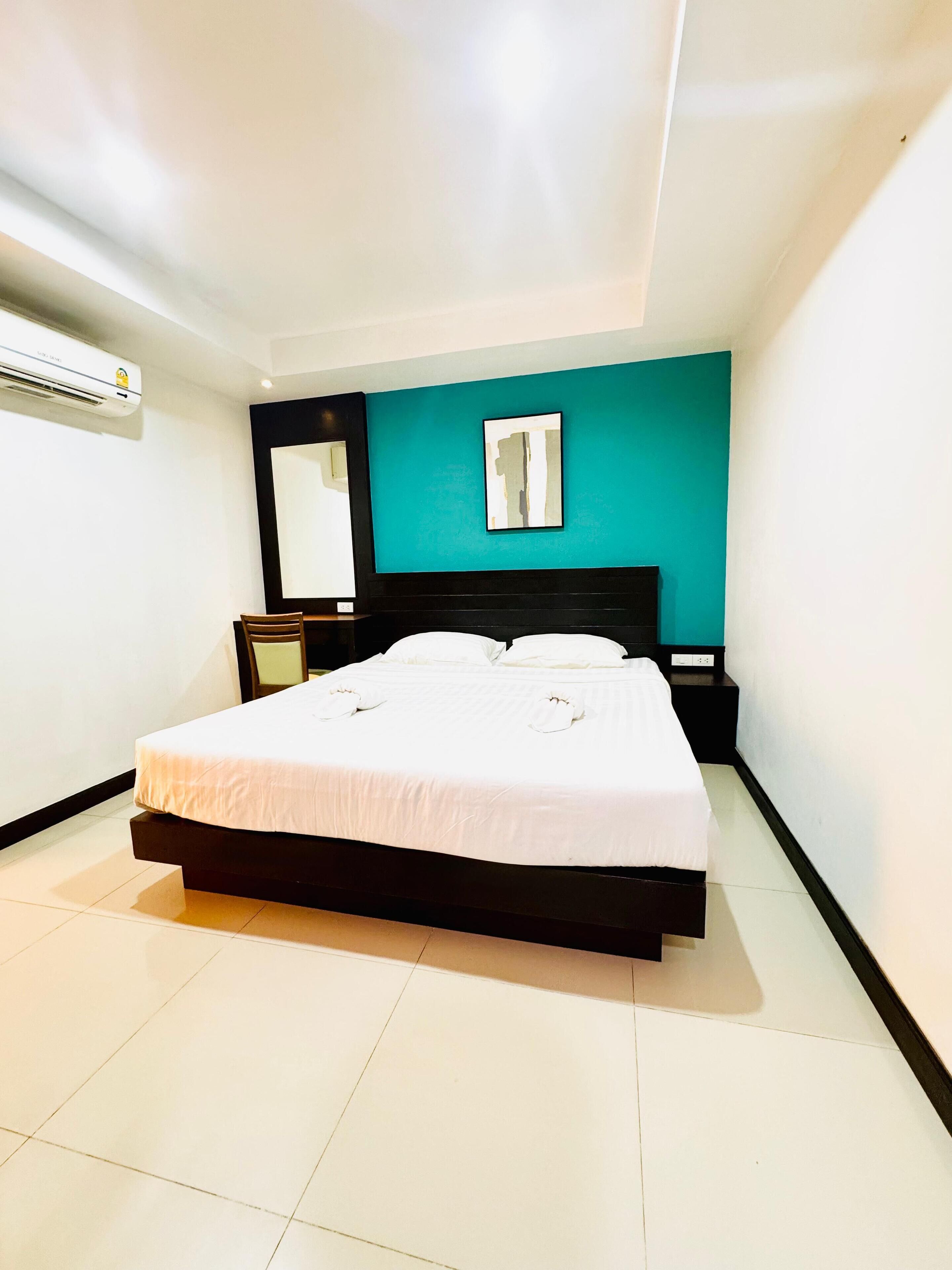A modern bedroom with a large bed, a nightstand, a wall-mounted air conditioner, and a teal accent wall.