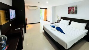 Une chambre d’hôtel avec un lit, un bureau avec une télévision, un climatiseur et une fenêtre avec des rideaux.