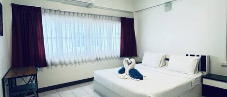 Une chambre d’hôtel comprenant un lit, un bureau, une chaise, une fenêtre avec des rideaux, un appareil de climatisation et un sol carrelé.