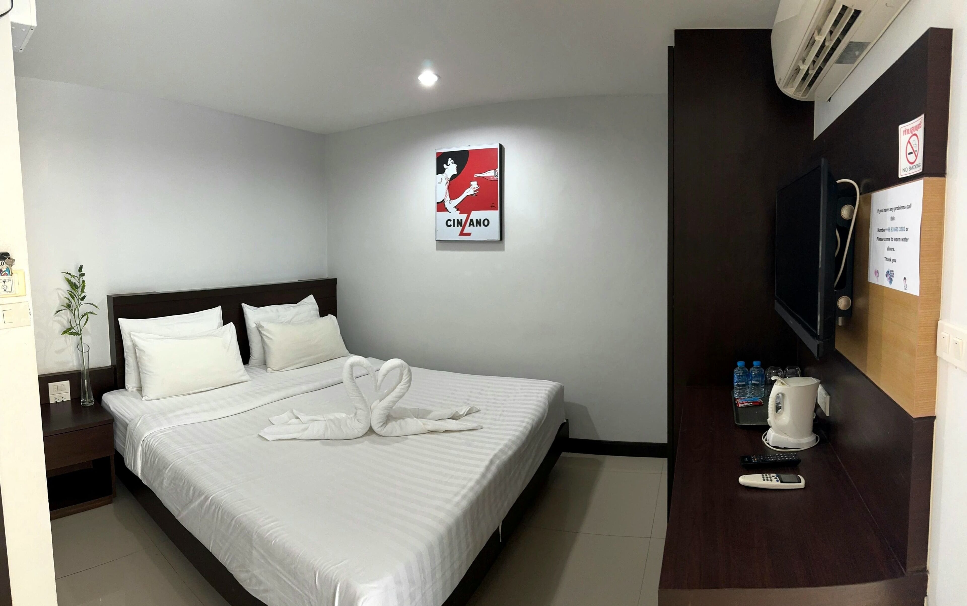 A hotel room with a neatly made bed, a wall-mounted TV, a coffee maker, and a poster on the wall.