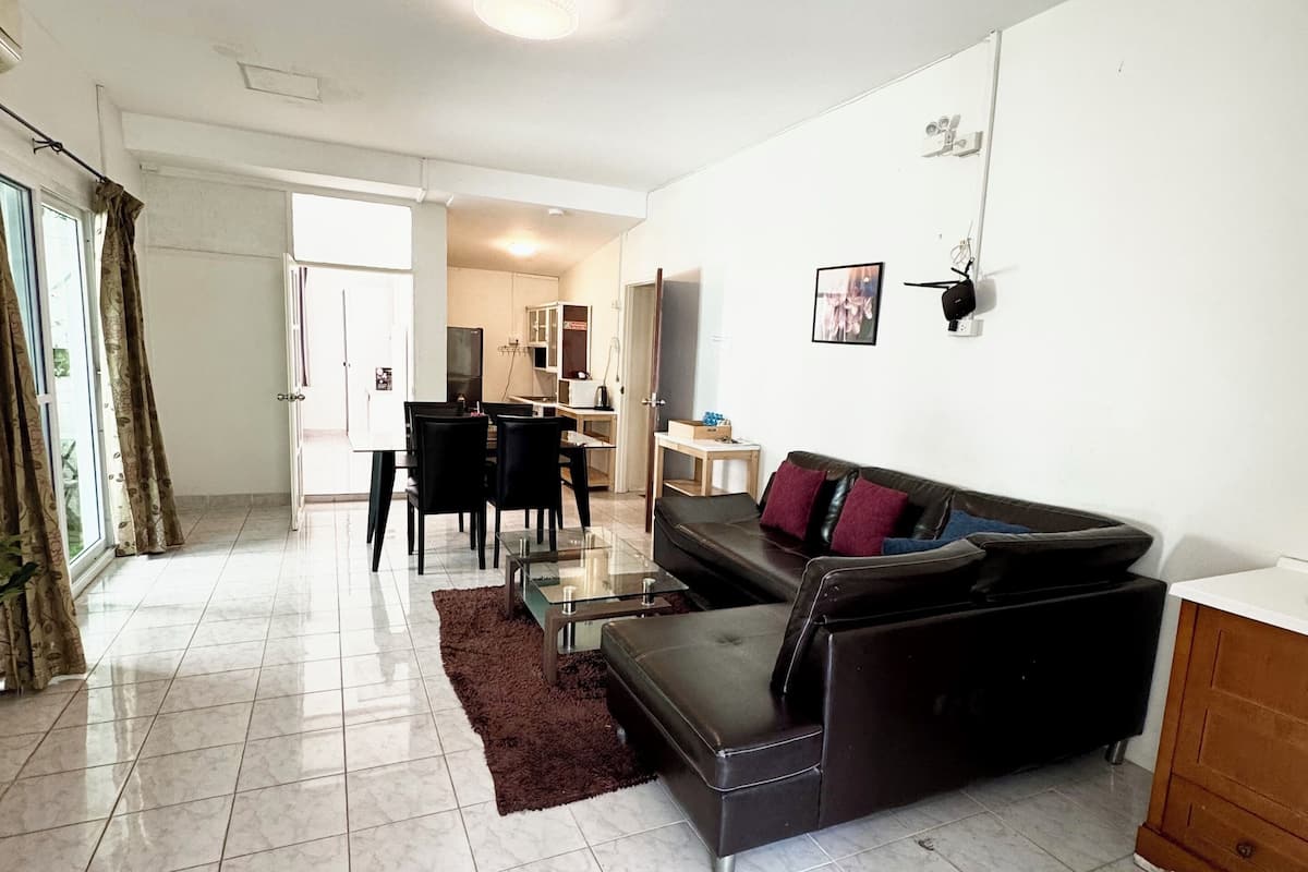 Uma sala de estar ampla com um sofá de couro preto, uma mesa de centro de vidro e um espaço de jantar com mesa e cadeiras.