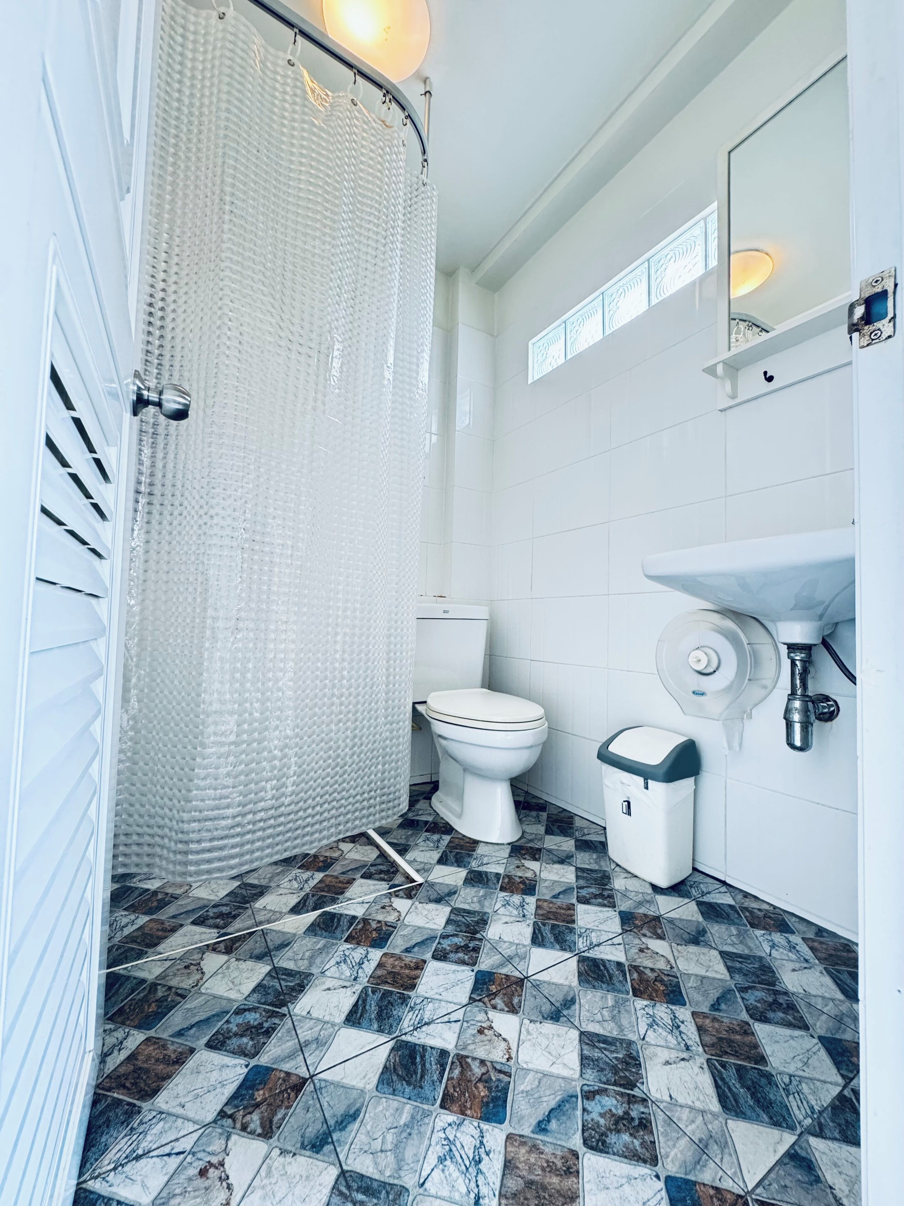 A bathroom with a shower curtain, toilet, sink, and tiled floor.