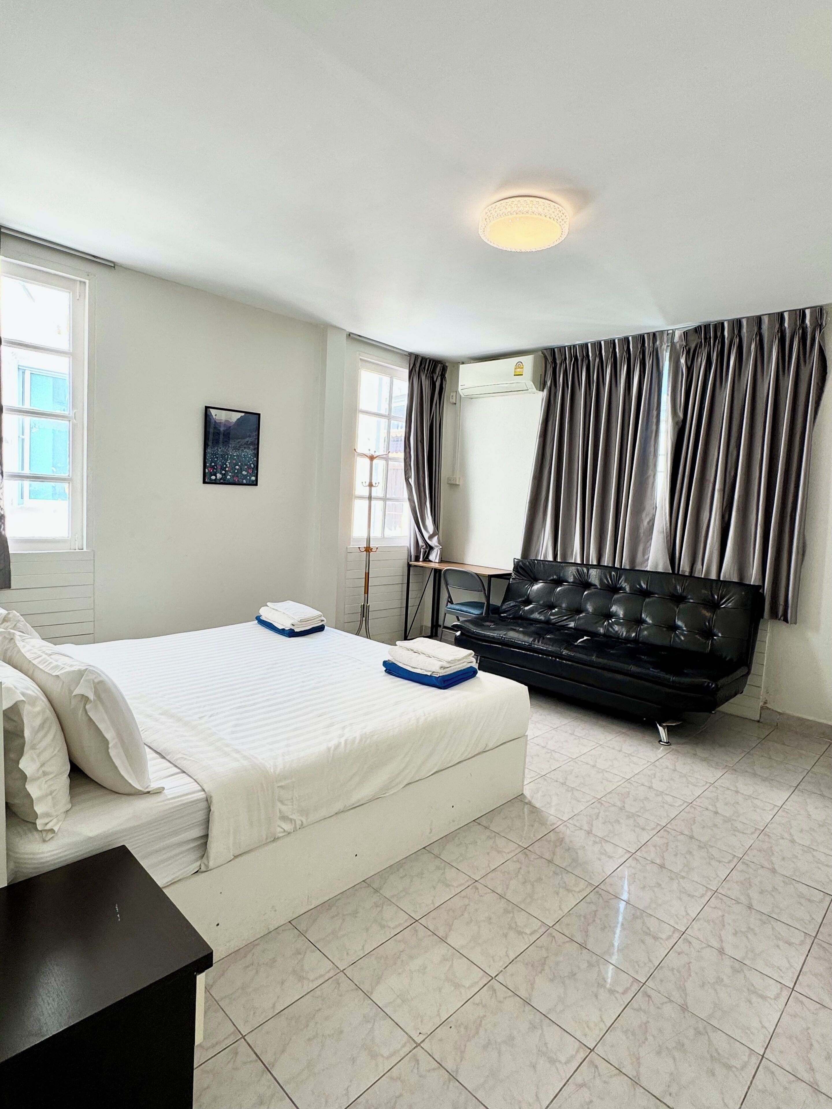 A hotel room with a bed, a black leather sofa, a picture on the wall, and a window with curtains.