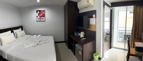 Habitación de hotel con cama, escritorio con televisor, minibar y vistas al balcón exterior.
