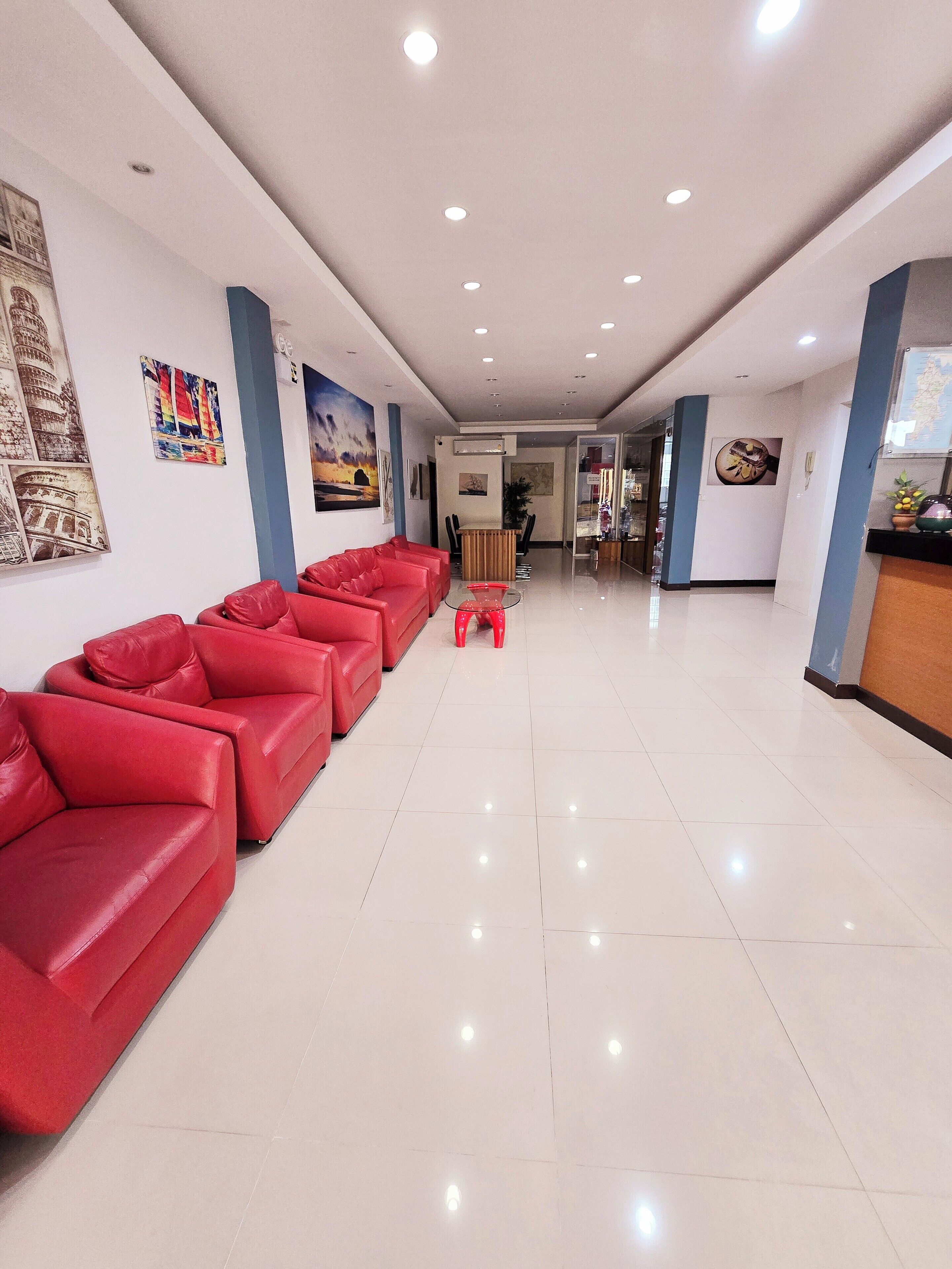 Um hall amplo com sofás de couro vermelho, um balcão de recepção e piso ladrilhado.