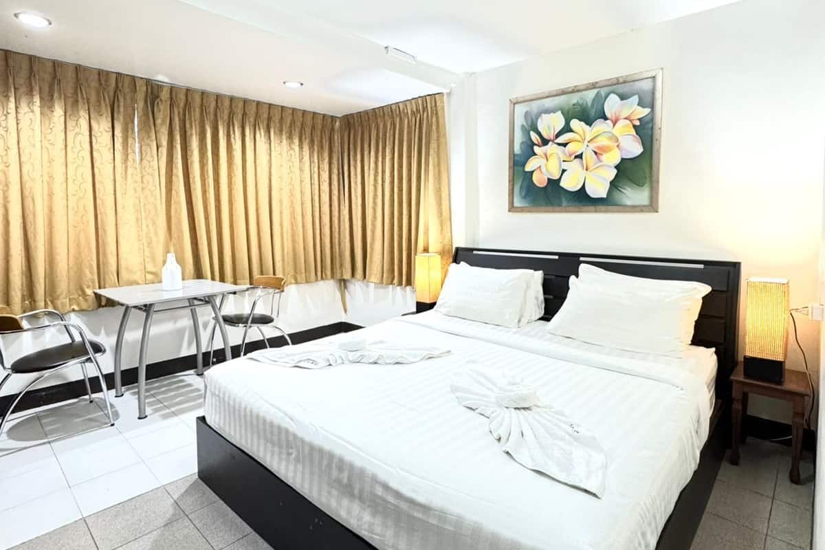 Quarto de hotel com uma cama grande, uma escrivaninha com cadeiras, um quadro de flores na parede e uma luminária no teto.
