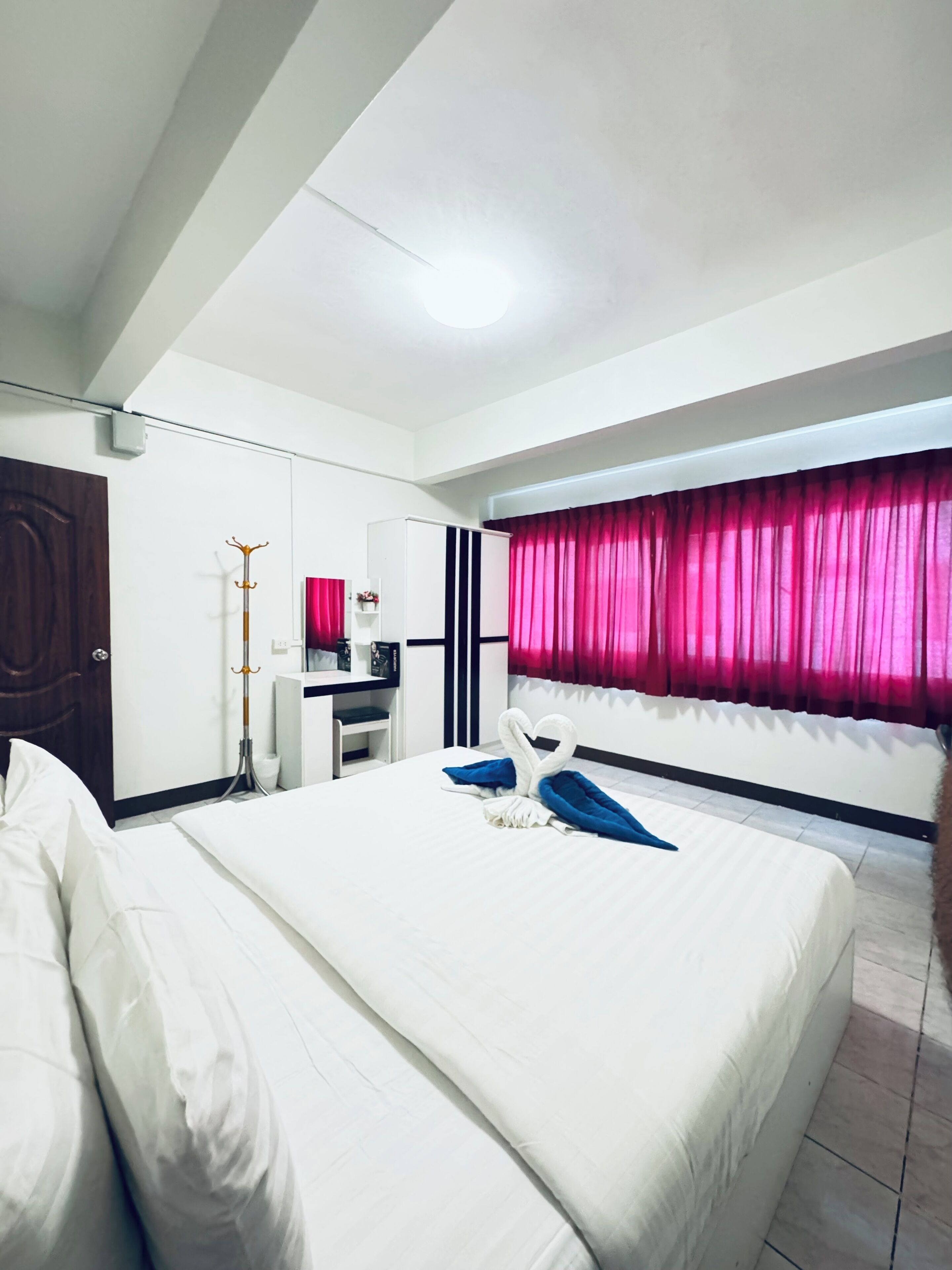 A hotel room with a large bed, a desk, a wardrobe, and a window with curtains.