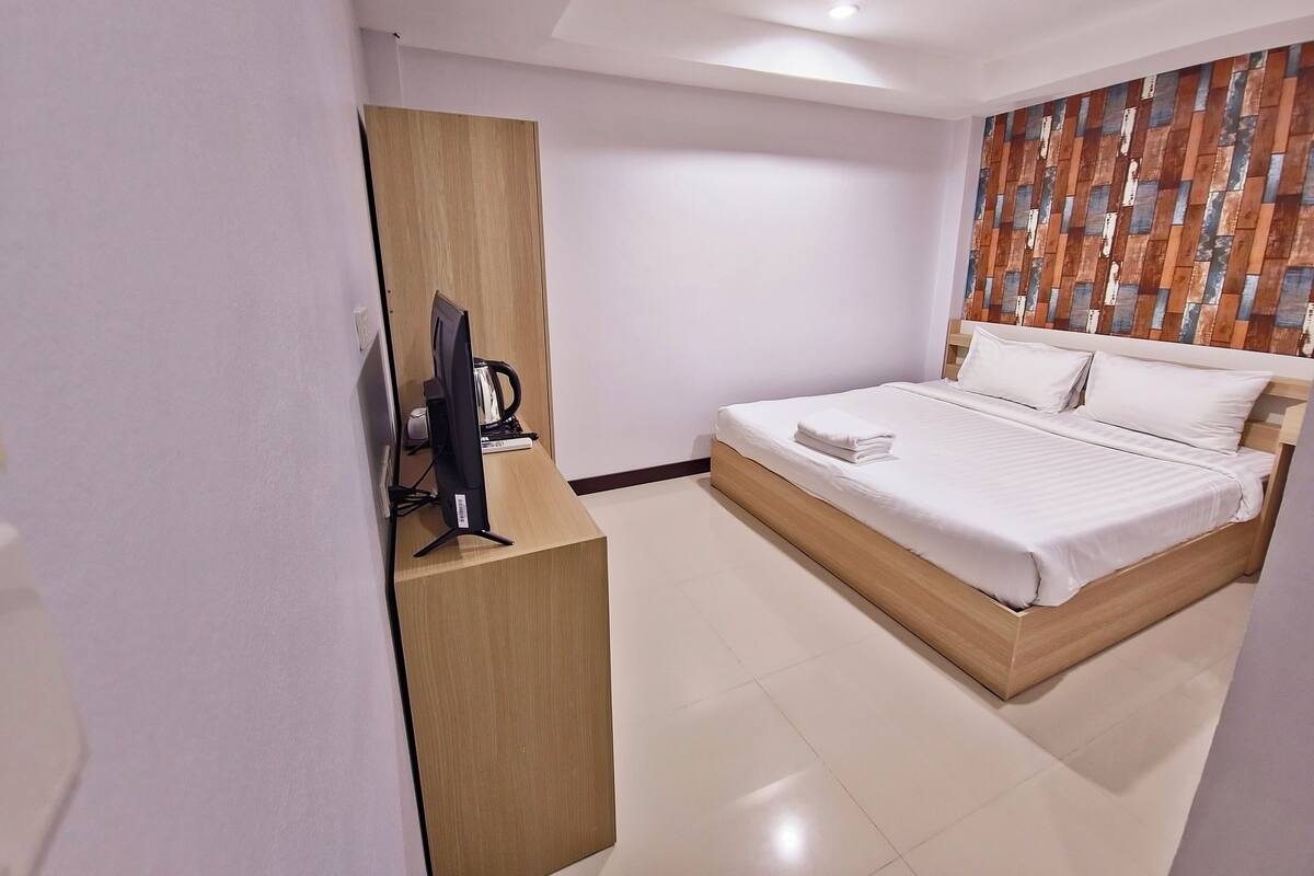 Quarto de hotel moderno com uma cama, uma secretária com um computador e um guarda-roupa de madeira.