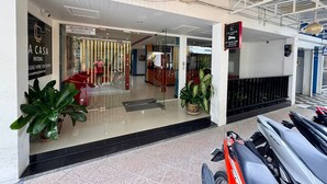 L’entrée d’un hôtel, avec une façade en verre, un comptoir d’accueil et une enseigne indiquant « La Casa ».