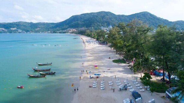 Une plage avec des bateaux, des parasols et une chaîne de montagnes en arrière-plan.