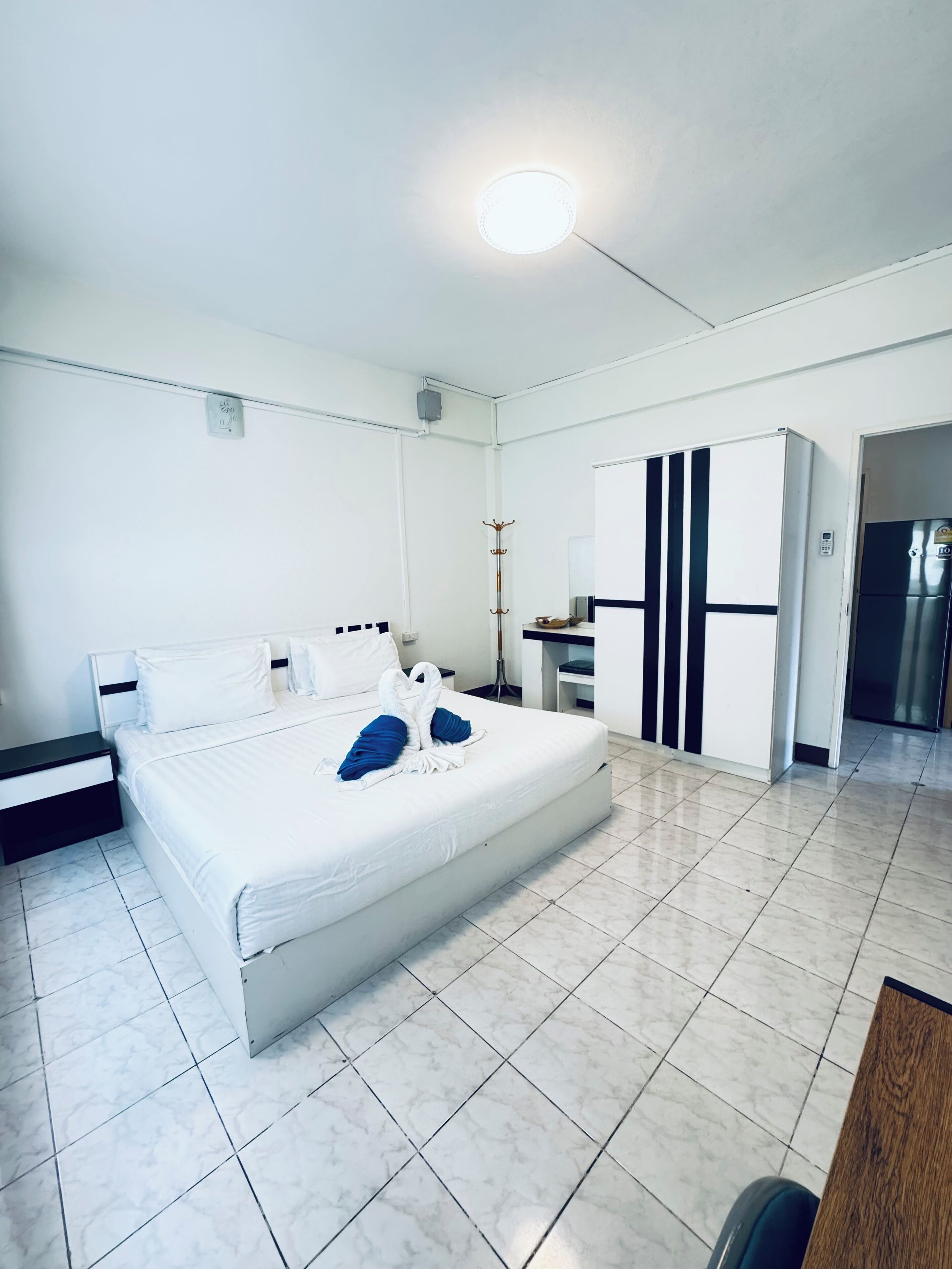 A modern hotel room with a large bed, a wardrobe, a desk, and a mirror.