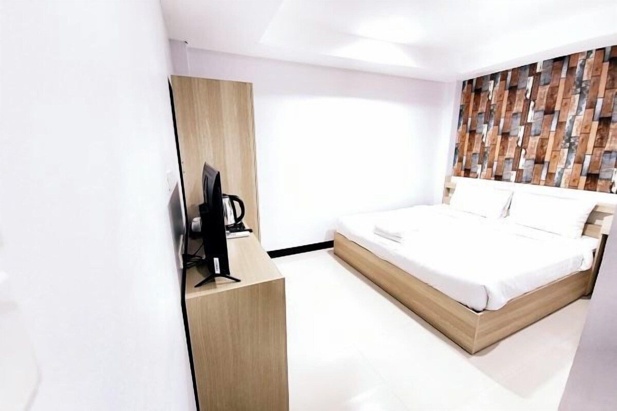 A modern hotel room with a wooden bed frame, a flat-screen TV on a wooden desk, and a patterned wall.