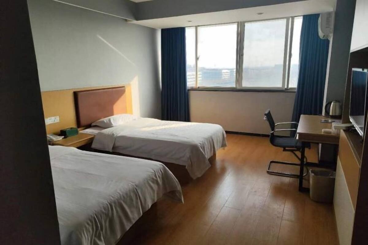 A hotel room with two beds, a desk, a chair, and a window with curtains.