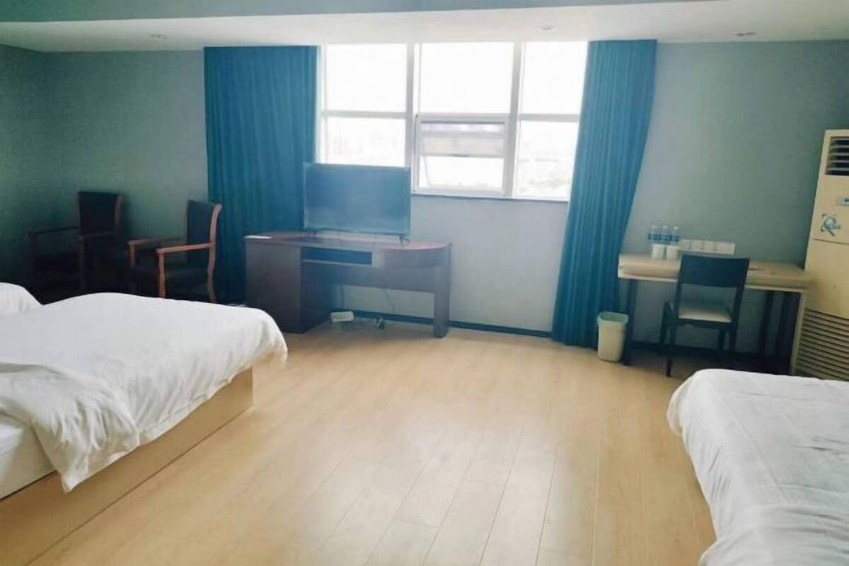 A hotel room with two beds, a desk, a chair, a TV, and a window with curtains.